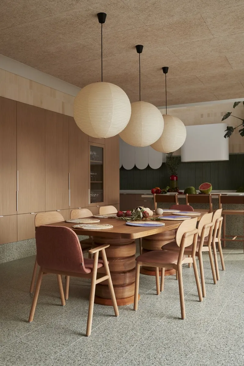 Dining room with curved timber table, paper globe pendants and green fluted backsplash beyond
