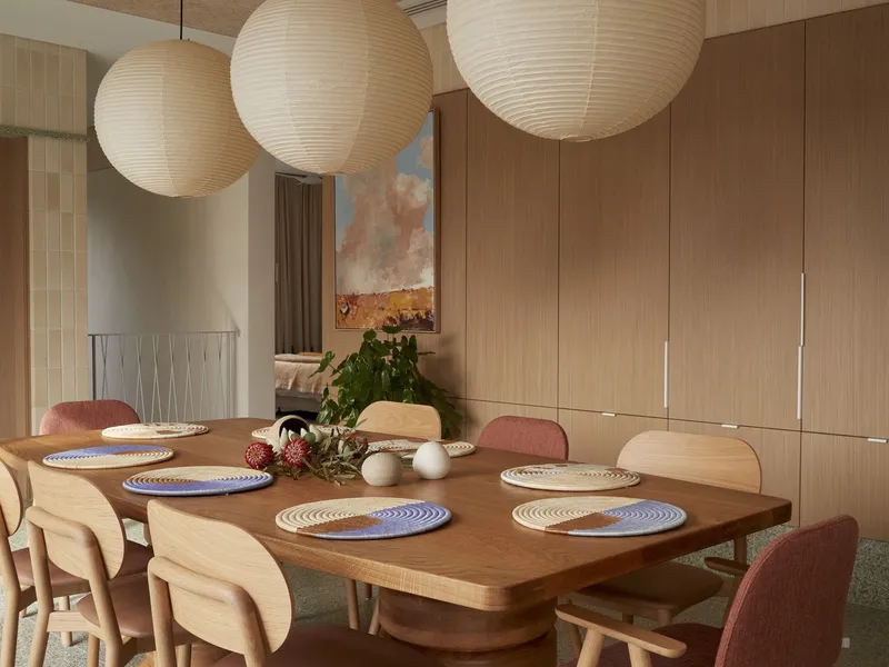 Dining room with timber table set for eight beneath three spherical paper pendant lights