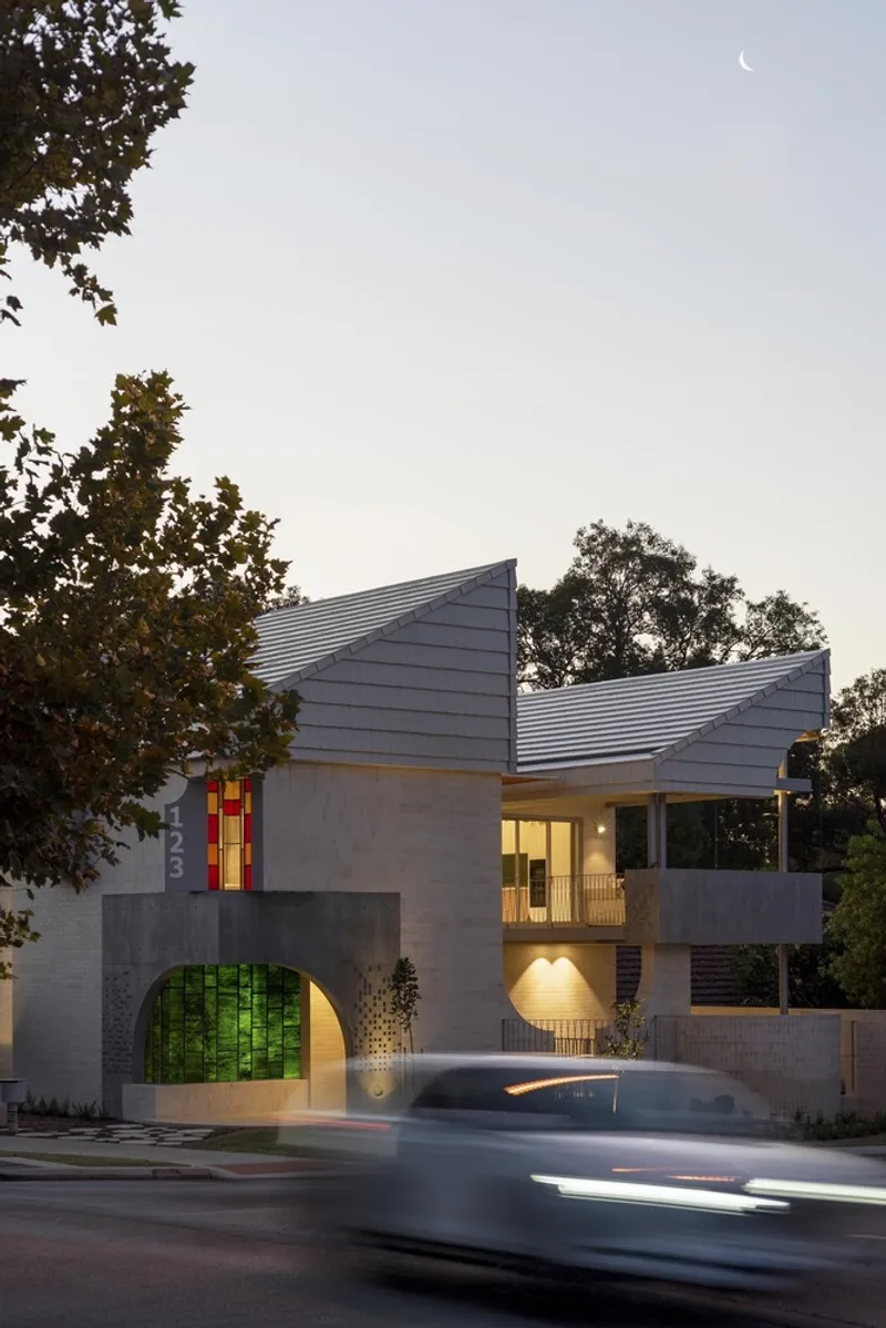 Street view of the folded metal roof and concrete facade at dusk with car passing