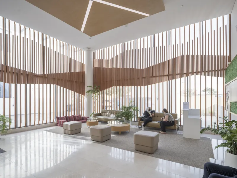 Double-height lobby with vertical timber brise-soleil filtering daylight across polished white floor