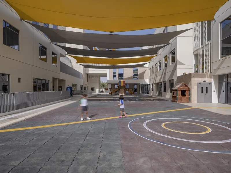 Courtyard with concentric circle paving markings and two children walking beneath tensile canopies