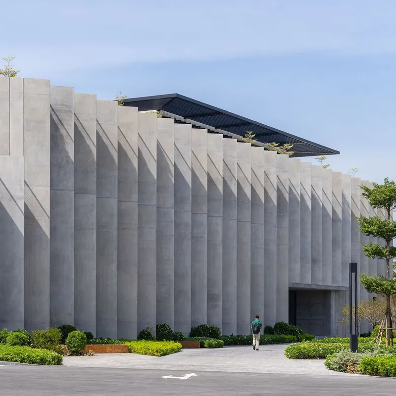 Vertical concrete fin facade with a visitor approaching the entrance through landscaped grounds