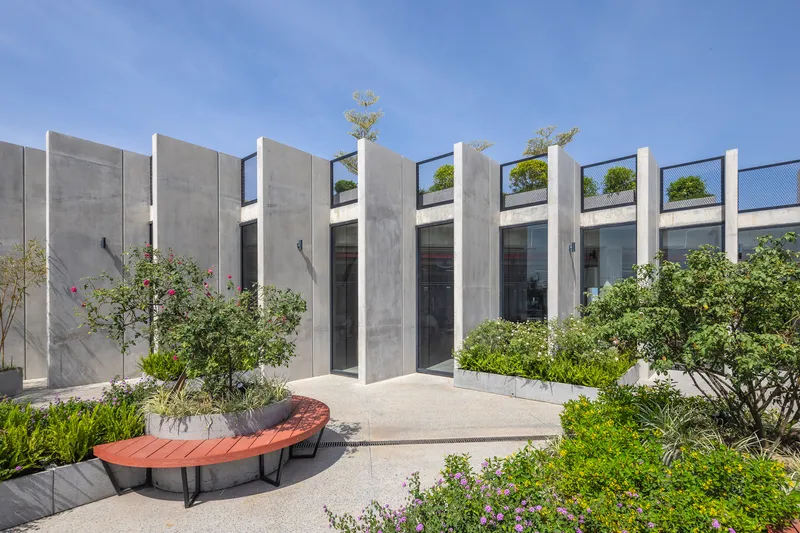 Ground-level view of concrete fin facade with glazed openings and curved red bench among planted beds
