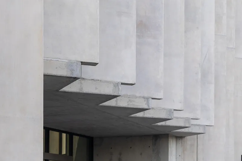 Close-up of concrete sawtooth canopy overhang with exposed structural soffit above glazed opening