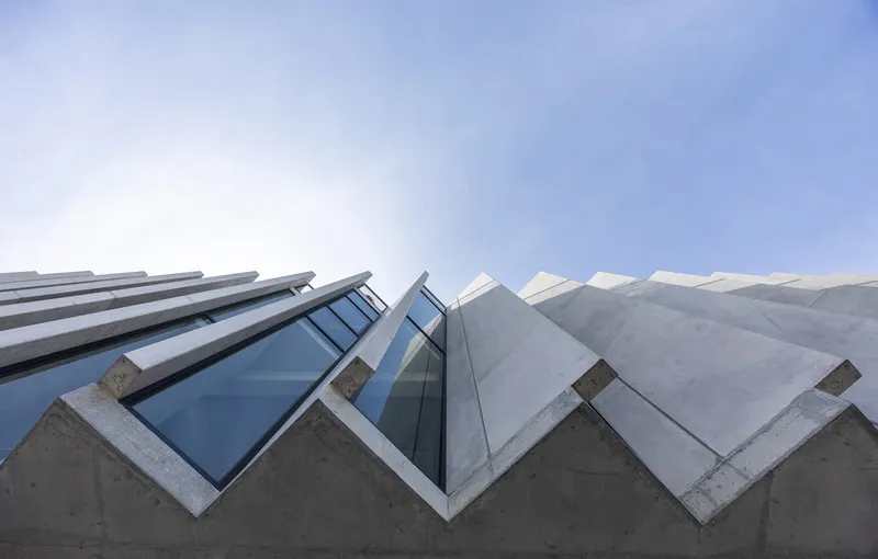Worm's-eye view of angled concrete and glass facade against a bright sky
