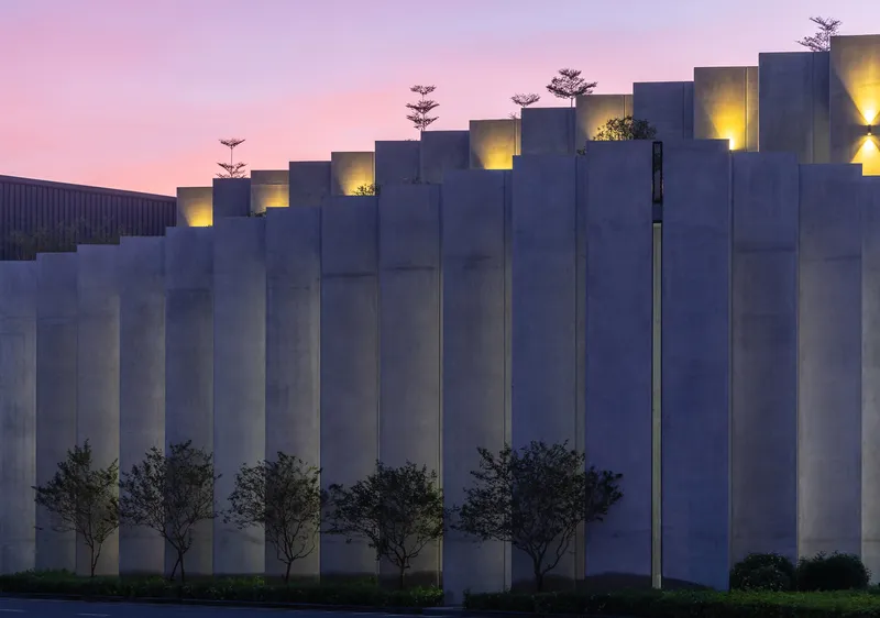 Stepped concrete facade with vertical fins and recessed uplighting beneath a pink dusk sky