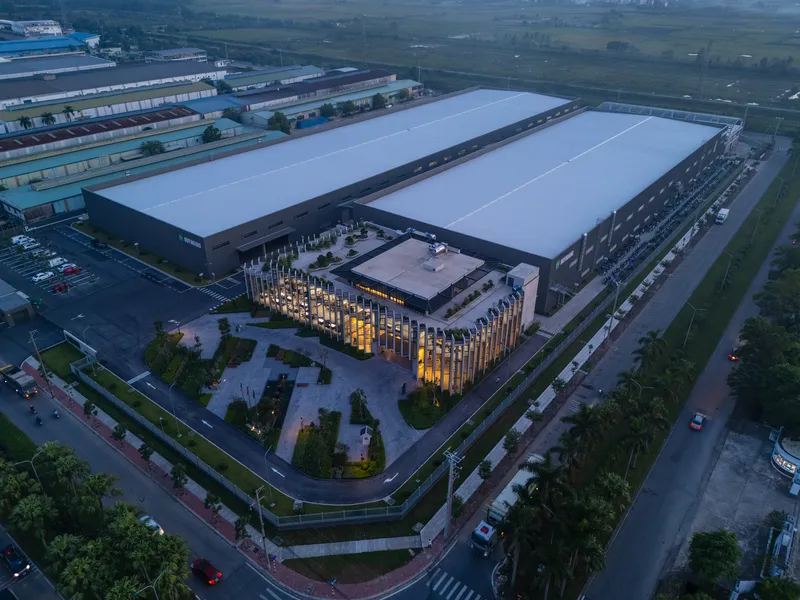 Aerial view of an industrial complex with warehouse roofs and illuminated vertical-finned entrance pavilion at dusk