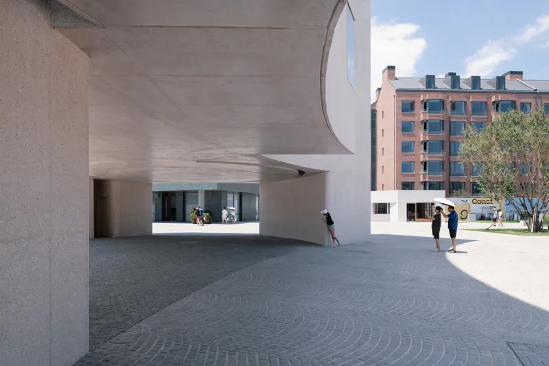 Covered entry plaza with curved concrete canopy sheltering visitors under patterned stone paving