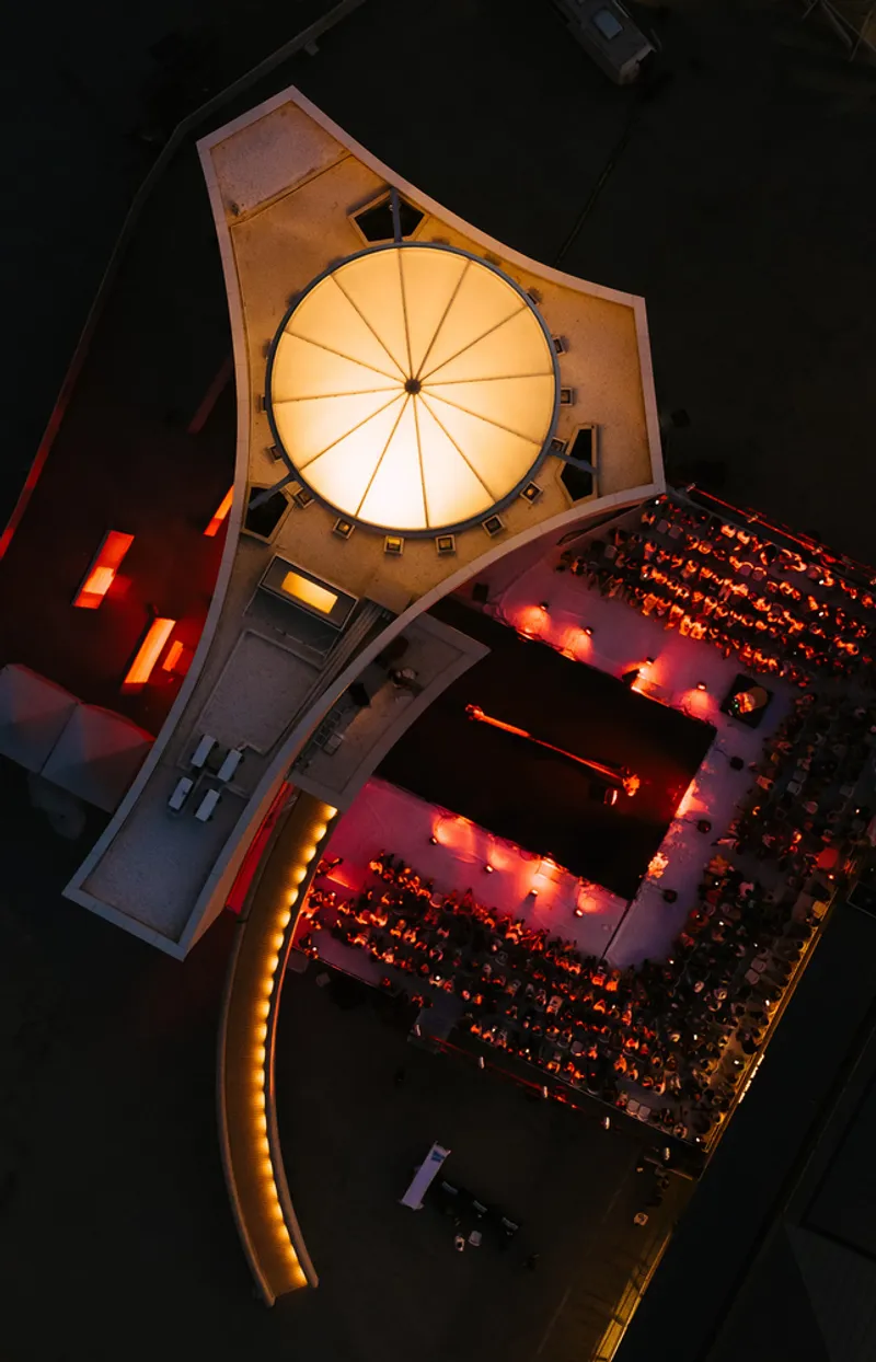 Aerial view of illuminated auditorium with radial ceiling and curved seating filled with audience at night