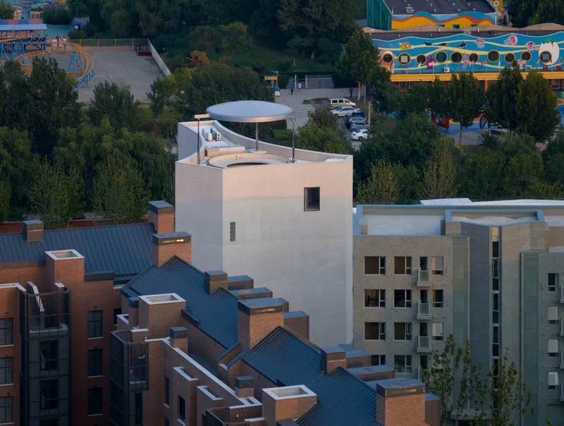 Rooftop view showing disc-shaped canopy atop tower volume among residential buildings at dusk