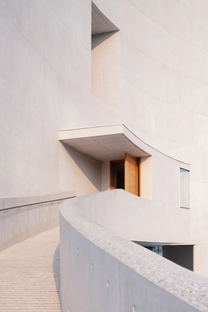 Close-up of recessed entry with timber door beneath angled concrete overhang and curved ramp