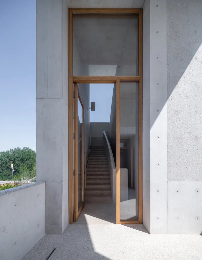 Timber-framed glass door opening to concrete stairwell in bright midday sun
