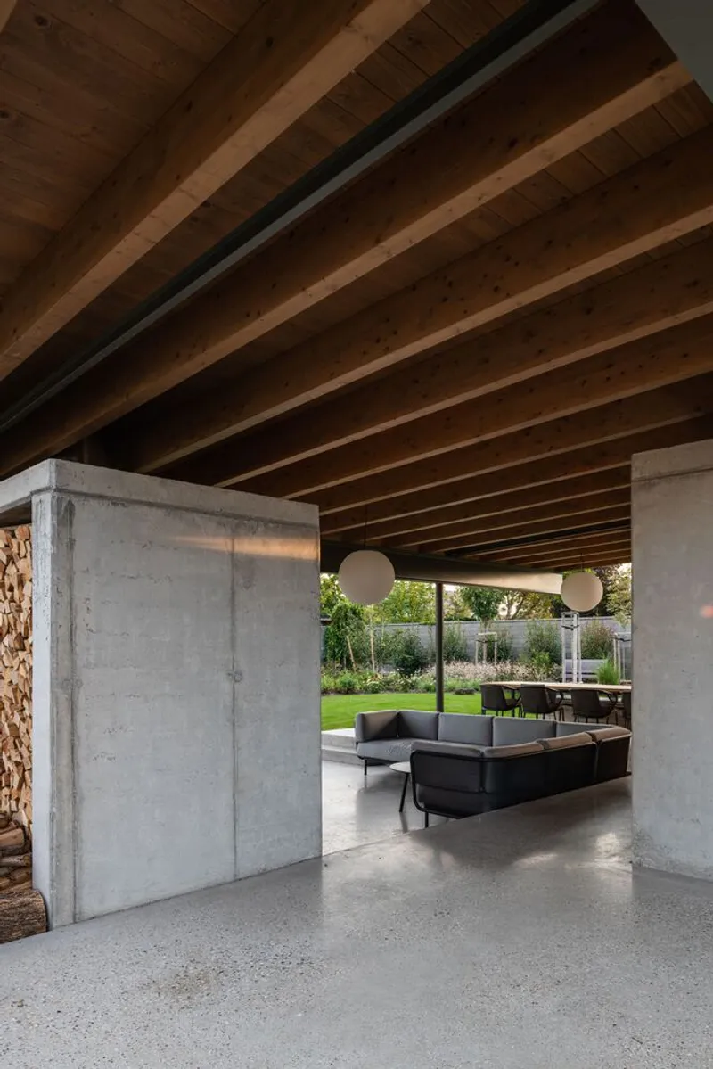 Interior view of exposed timber joists and steel beam above concrete columns with lounge seating and garden beyond