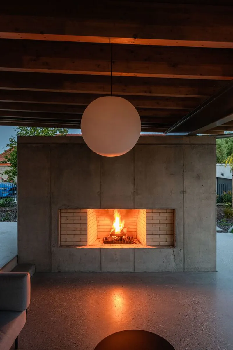 Concrete fireplace wall with brick firebox and spherical pendant light under exposed timber ceiling at night