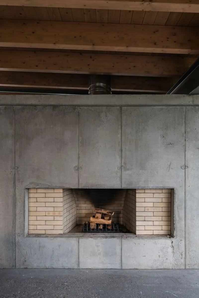 Detail of concrete wall with recessed brick-lined firebox opening beneath timber beam ceiling