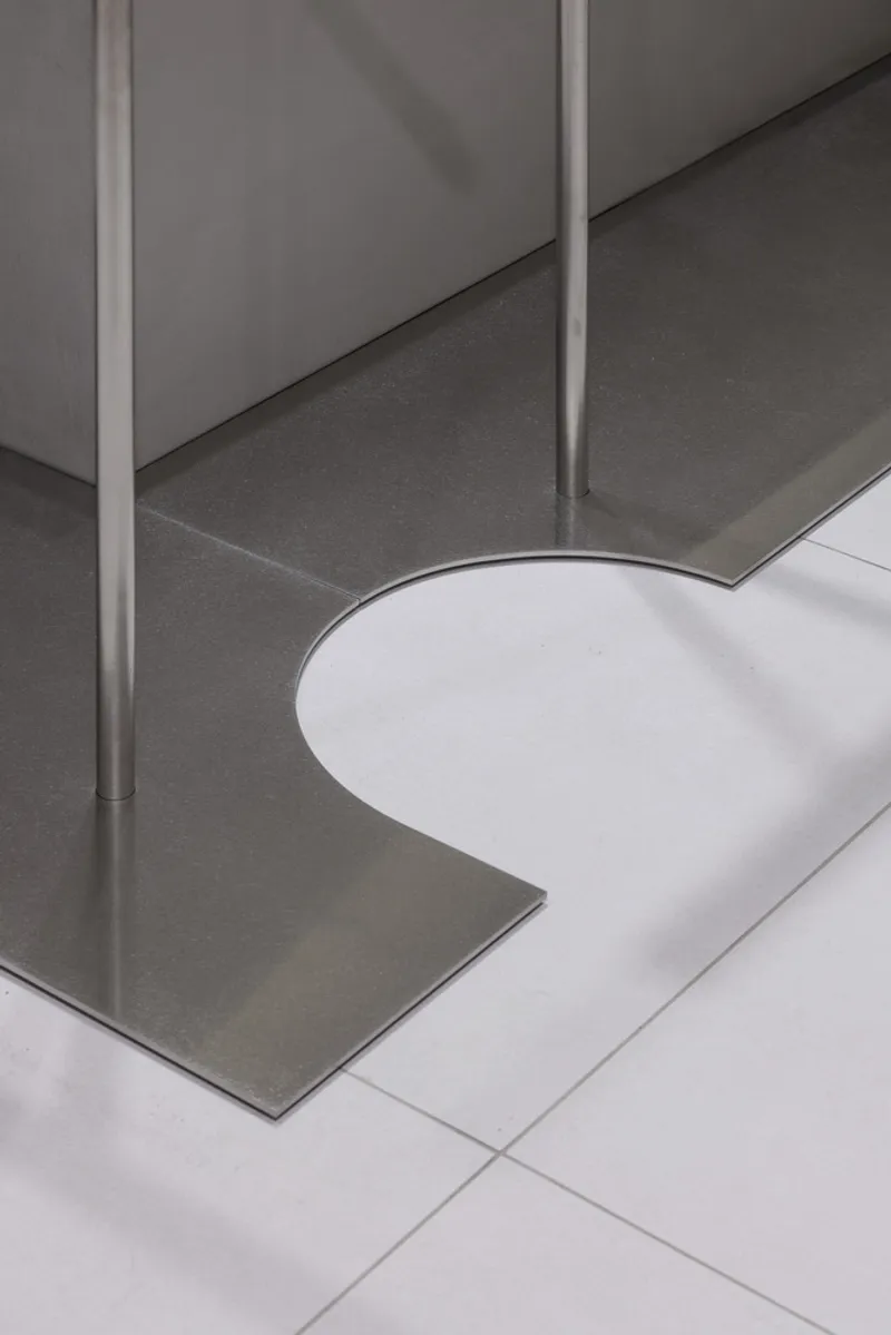 Detail of metal pole anchored in dark platform base meeting white tiled floor