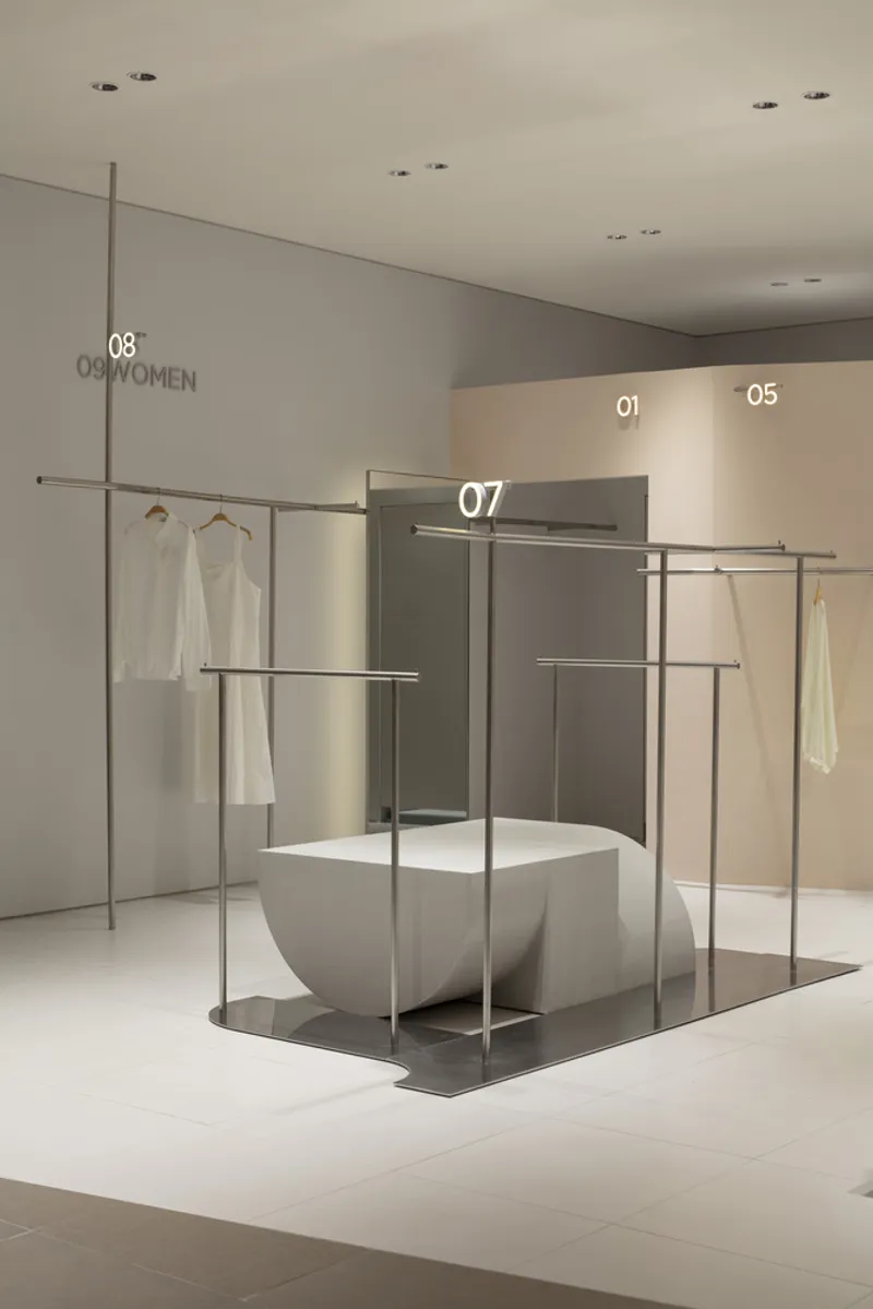 Display island with white sculptural seating element enclosed by slender metal garment rails