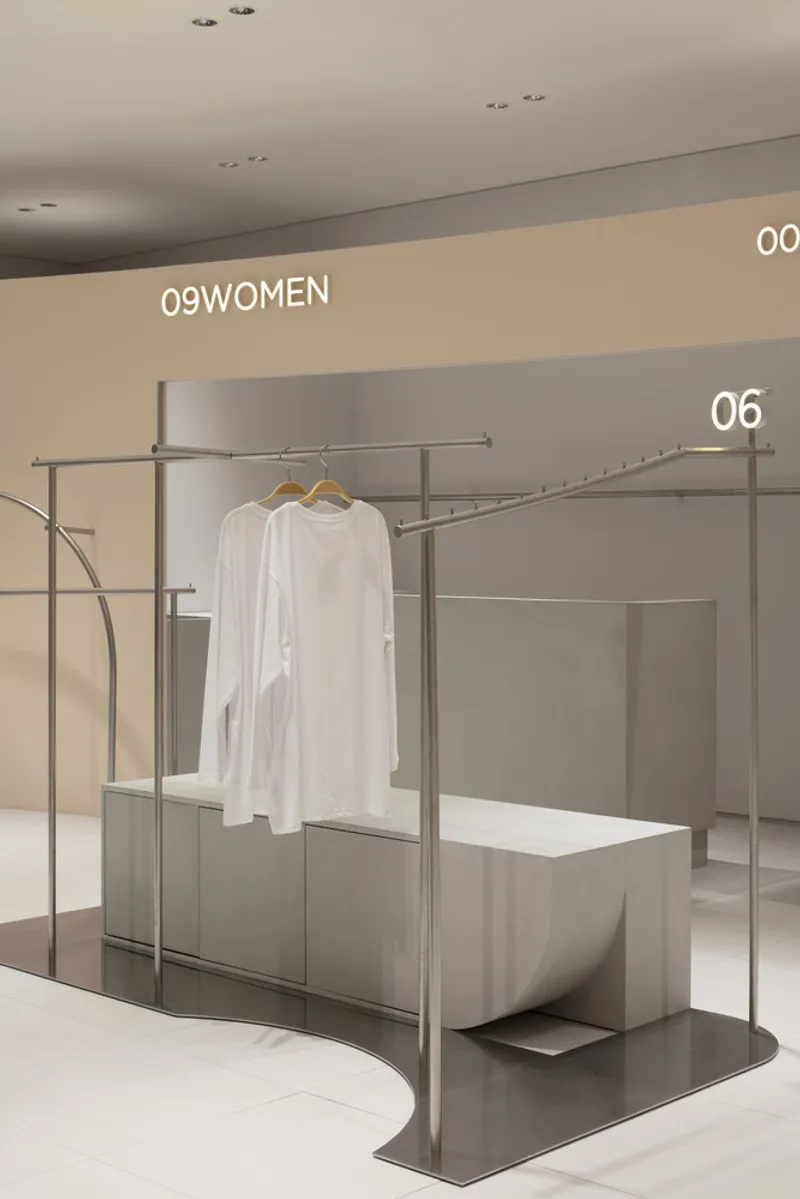 Single display unit with tubular steel frame holding white garments above a concrete base