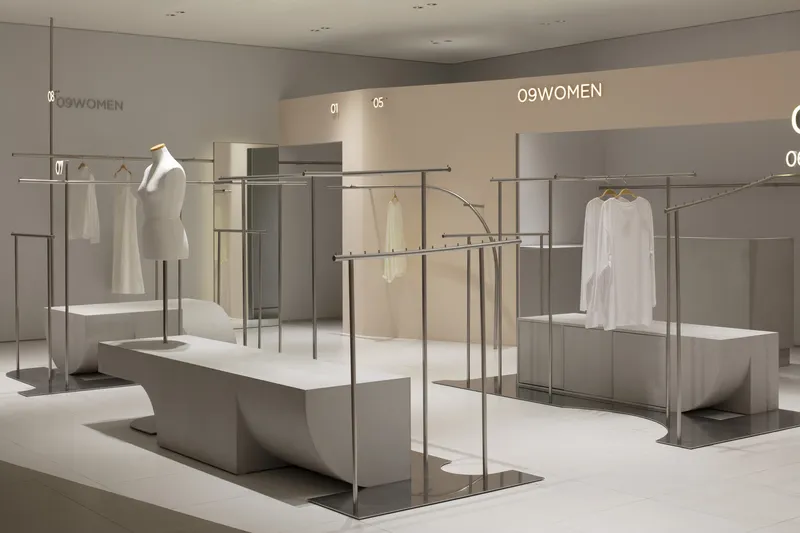 Clothing racks with curved steel frames and white garments on freestanding concrete plinths
