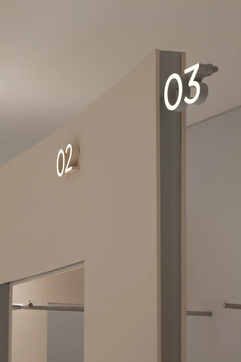 Illuminated numerical signage on beige walls beside doorways leading to retail fitting areas