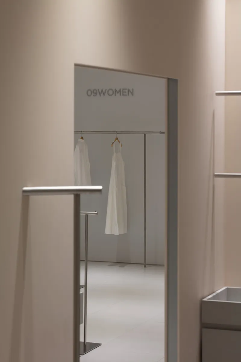 View through a doorway toward fitting rooms with white garments hanging on rail systems