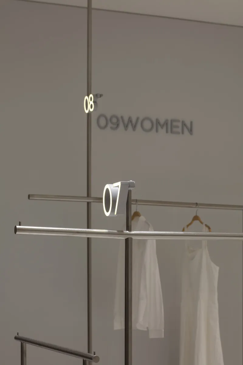 Overlapping metal rails with illuminated number signs and white garments on wooden hangers