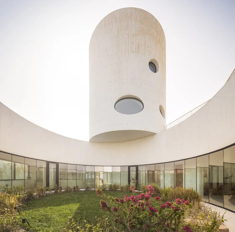 Circular courtyard garden with glass curtain wall below cantilevered concrete tower with oval windows