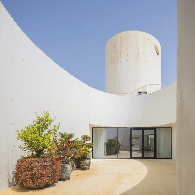 Courtyard with curved concrete walls, cylindrical tower above, and potted plants in afternoon sun