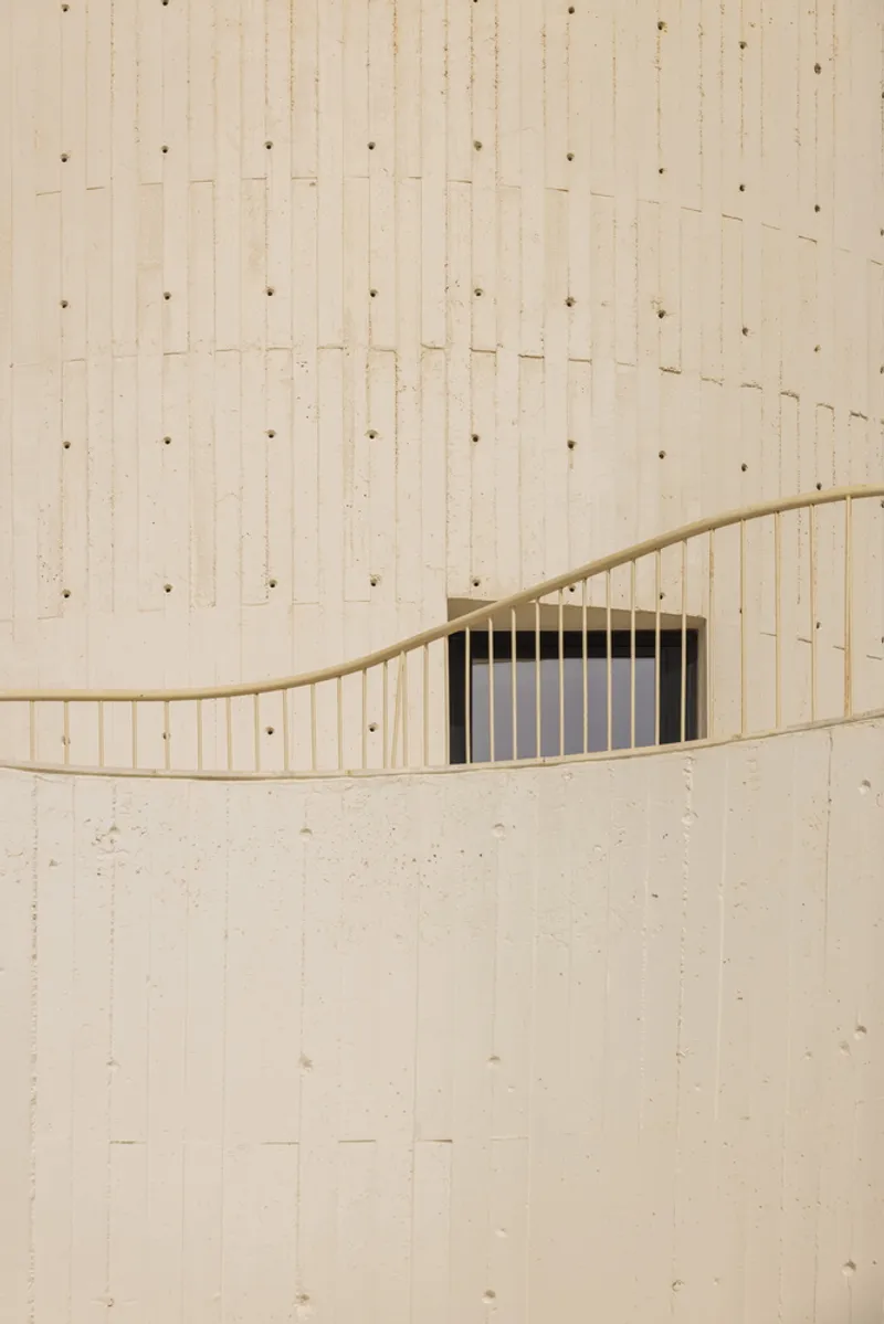 Close-up of boardmarked concrete wall showing undulating horizontal relief and recessed vertical glazing with bronze frame