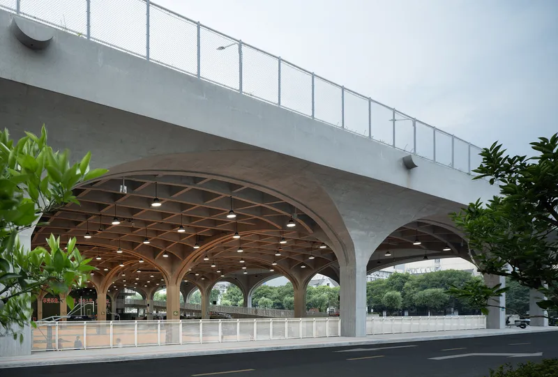 Street view of gridded timber vault beneath concrete podium with metal railing above