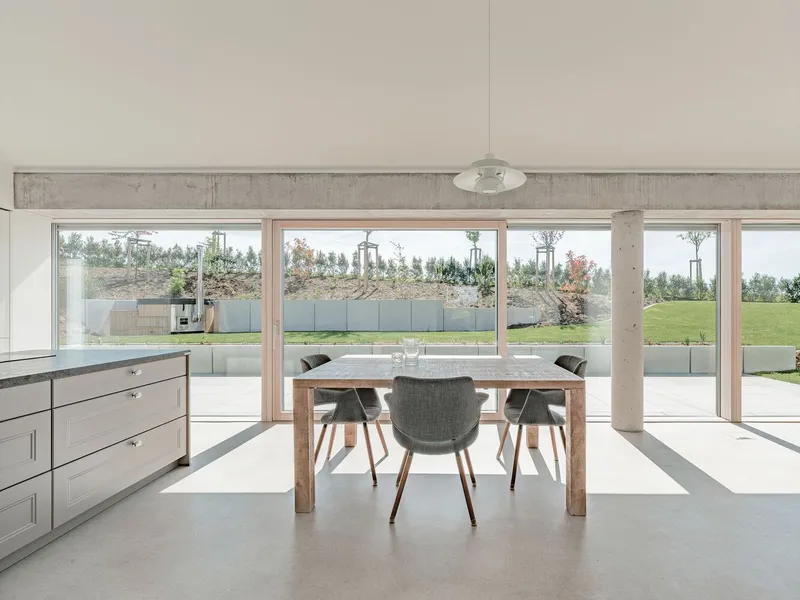 Dining area with exposed concrete beam and full-height glazing opening onto a terrace and lawn
