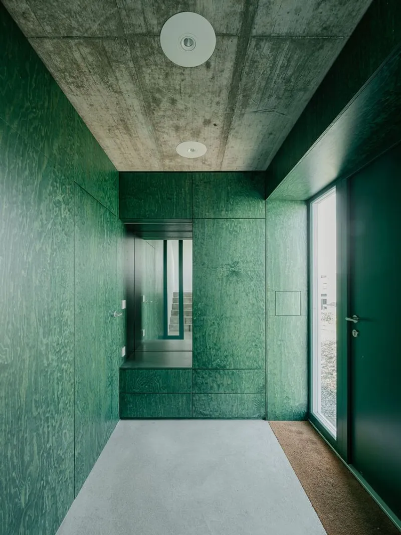 Entry hall clad entirely in teal-stained wood panels beneath an exposed concrete ceiling