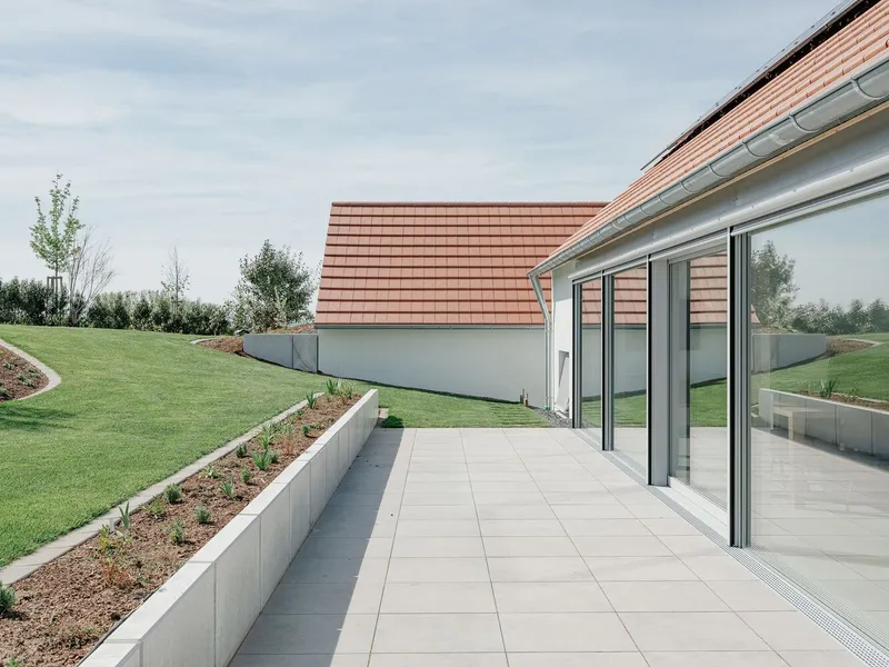 Terrace with large-format paving slabs bordered by a concrete planter bed and sloped lawn
