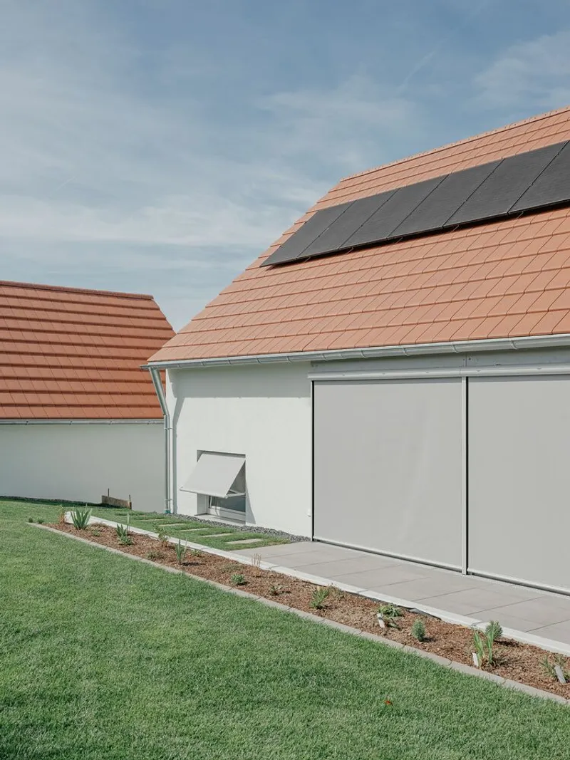 Clay tile roof with integrated solar panels above a white-rendered facade and planted slope