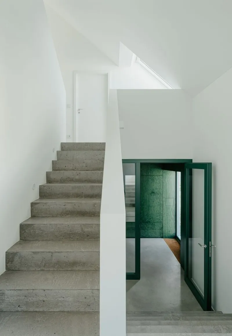 Concrete staircase rising alongside a doorway framed in teal-painted timber under sloped ceilings