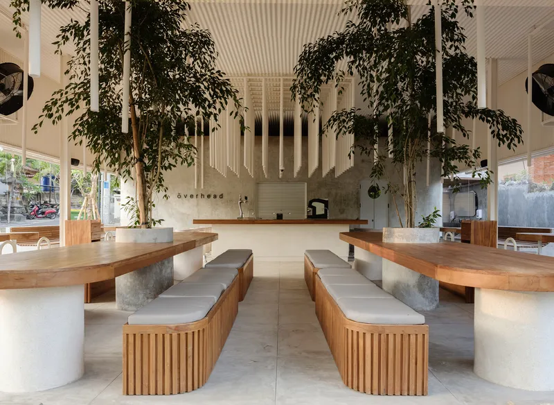 Interior dining space with timber bench seating and tall trees beneath a ribbed metal ceiling