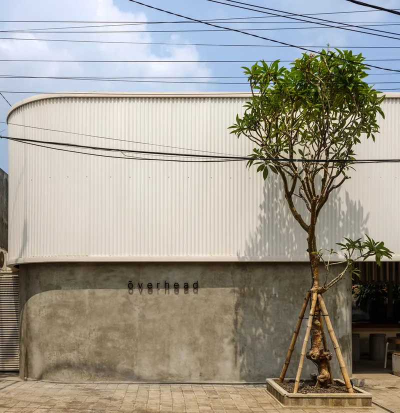 Street view of the curved corrugated metal facade above a concrete base with overhead power lines