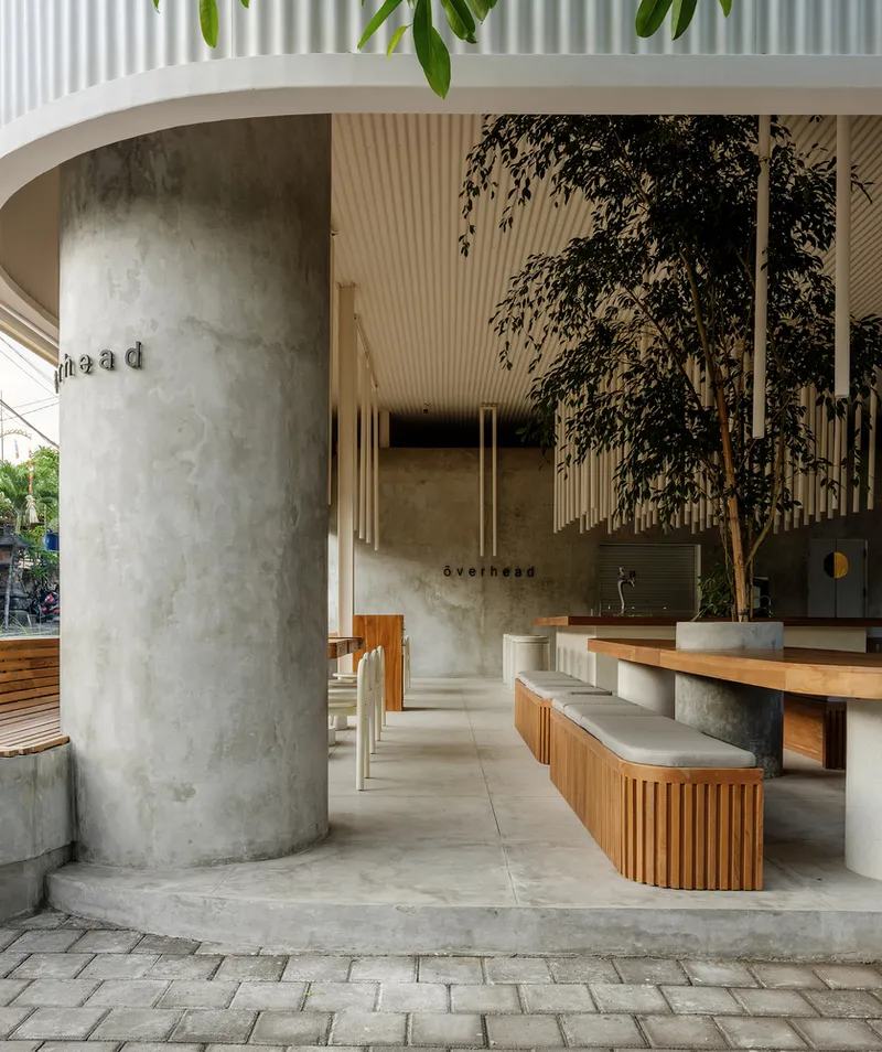 Semi-outdoor seating area with timber slatted benches and concrete planters beneath a corrugated ceiling