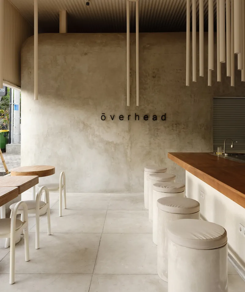 Interior counter with timber top and cylindrical white stools beneath suspended cylindrical light fixtures
