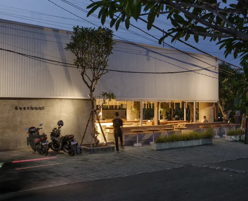 Evening view of the corrugated metal facade with lit interior visible through full-height glazing
