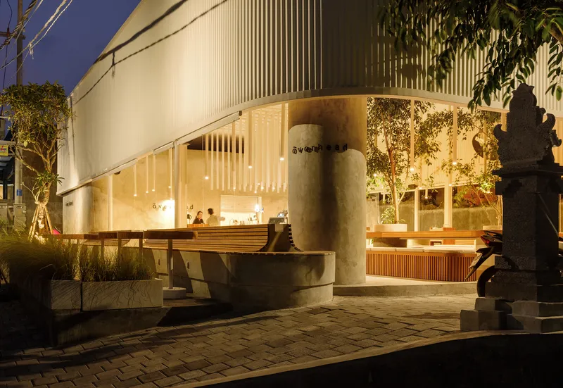 Evening view of the entrance courtyard with stone fountain, vertical louvers and interior dining visible through glazing
