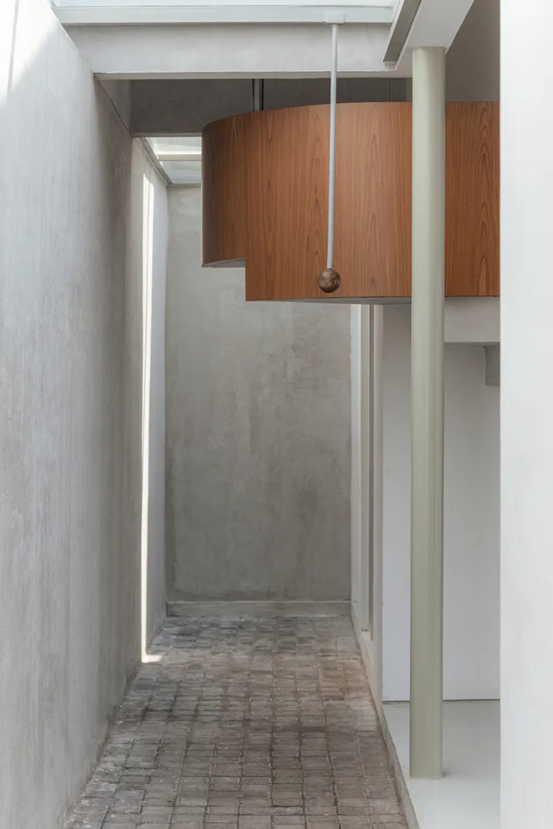 Narrow corridor with concrete walls, brick pavers underfoot and suspended walnut ceiling panels with hanging pendant