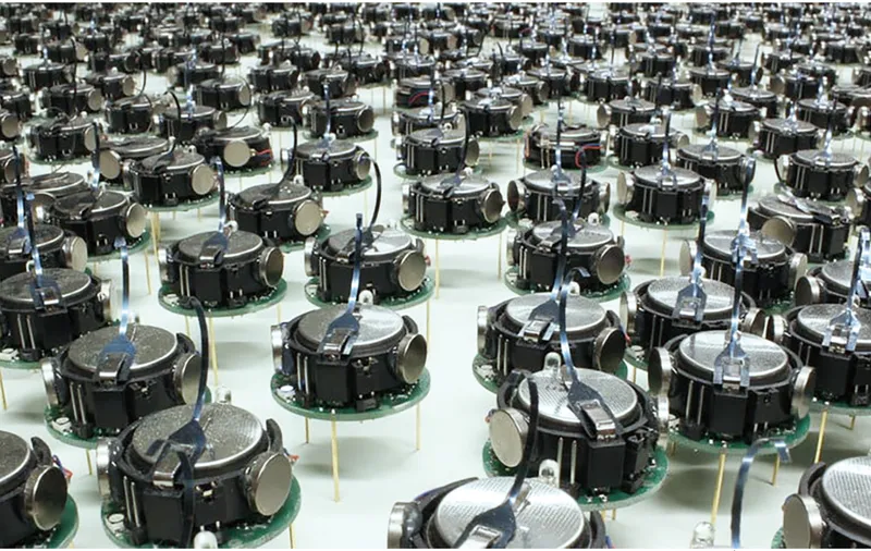 Array of black cylindrical robotic units arranged in rows on a white floor