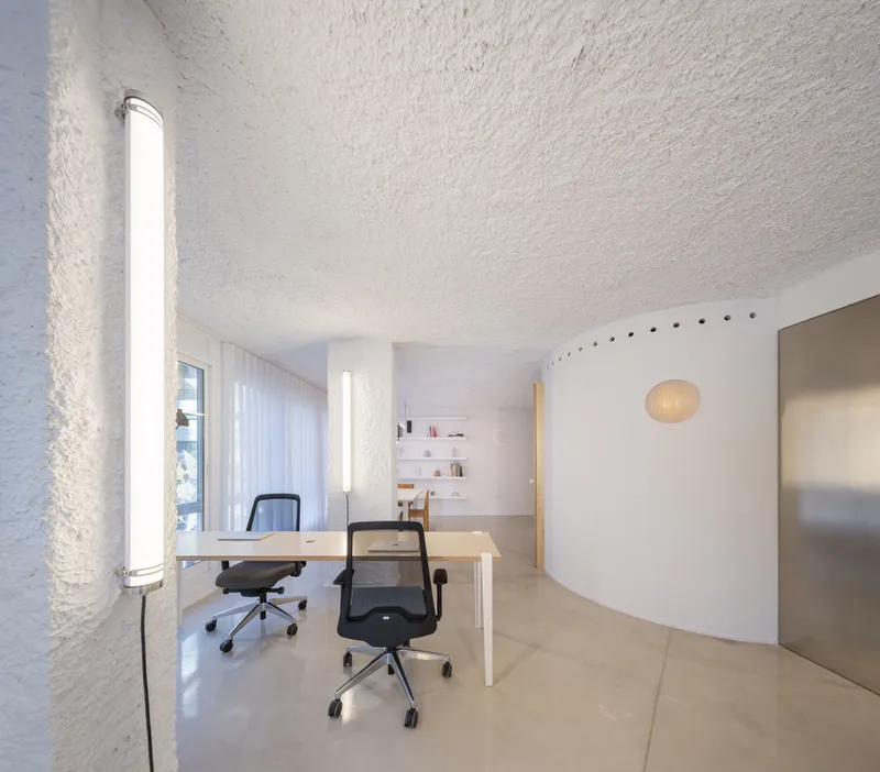 Office desk with two chairs under a tubular light fixture mounted on the textured wall