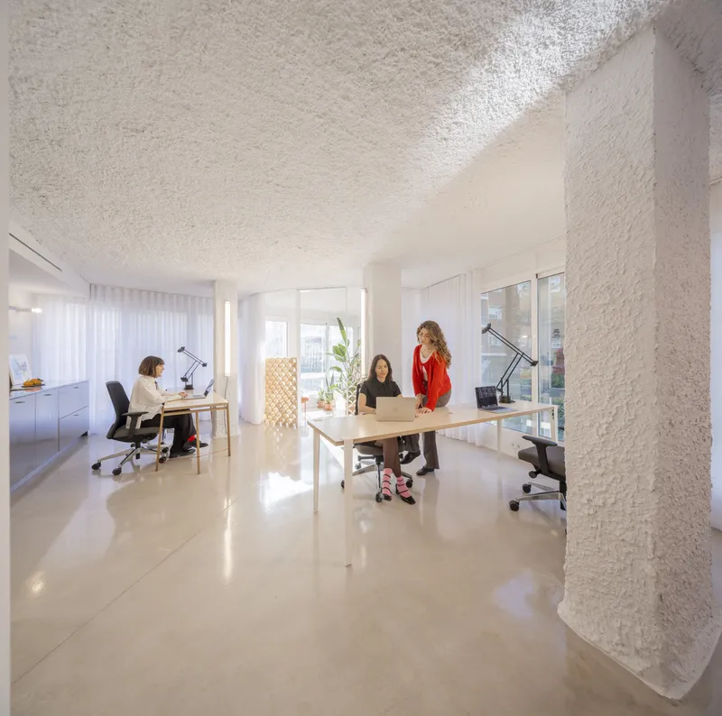 Open workspace with polished concrete floor, white textured ceiling and columns, and three people at desks