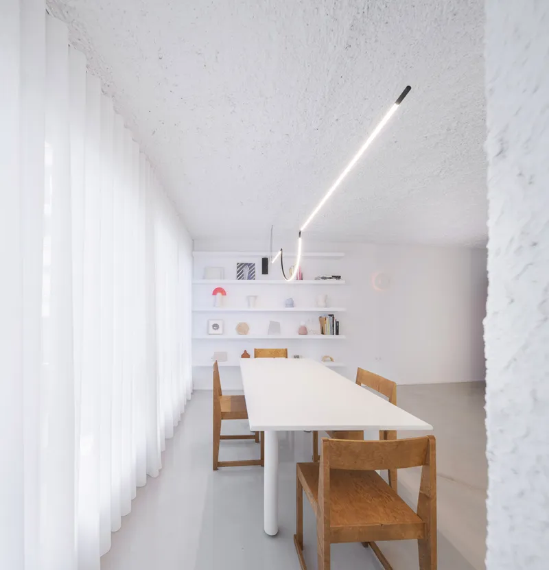 Meeting room with long white table, timber chairs, and articulated lighting fixture under textured vaulted ceiling