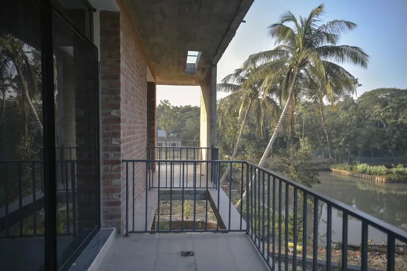 Balcony with metal railing overlooking a pond and palm trees in afternoon light