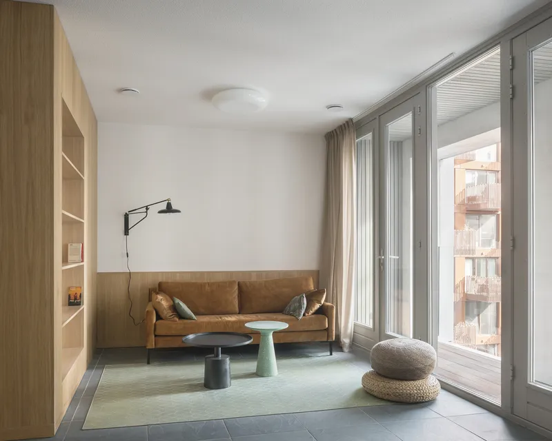 Living room with built-in timber shelving and glazed doors opening to a terrace with adjacent balconies visible