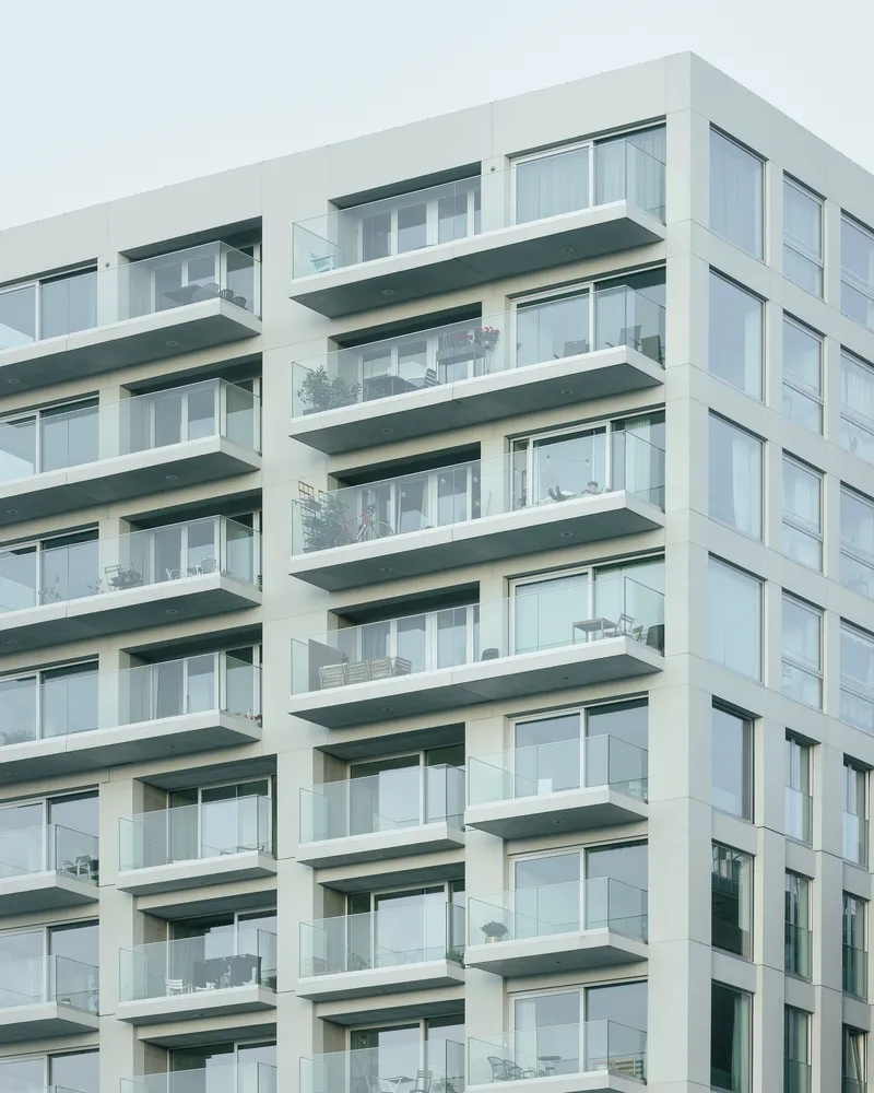 Facade detail showing stacked balconies with glass balustrades and dark soffit panels under overcast skies