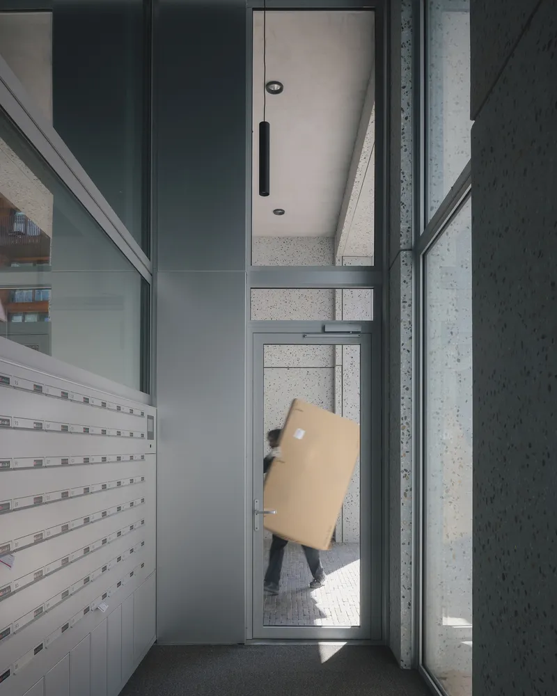 Narrow glass entrance corridor with a person carrying boxes through bright daylight